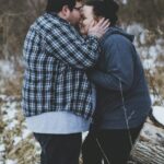 man kissing woman while standing near trees during daytime
